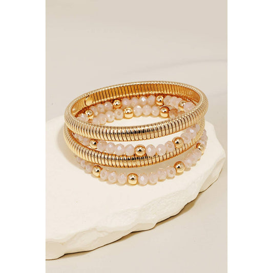 A stack of gold-colored metallic coil and beaded bracelets on a white cylindrical display stand.