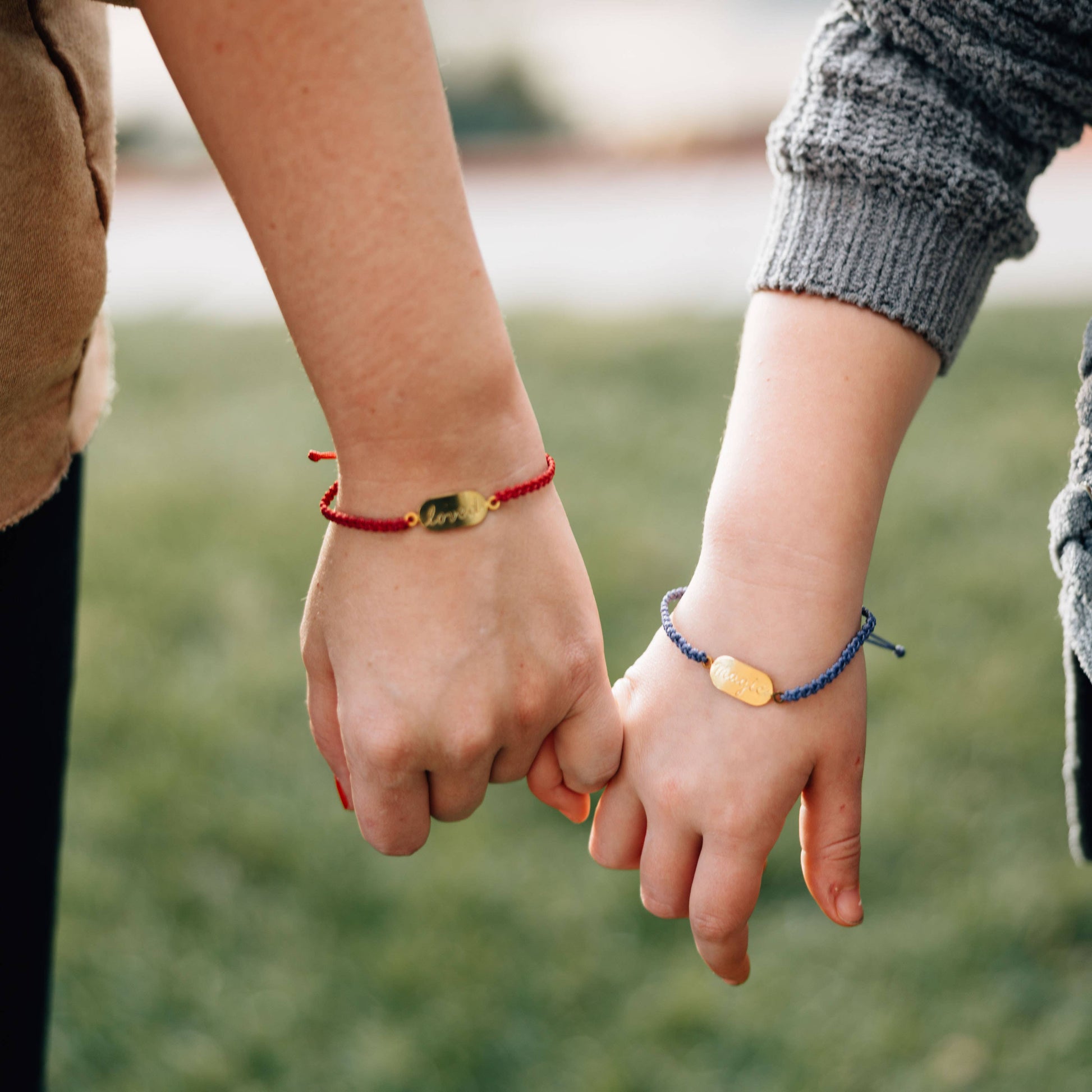 Two people holding hands with visible bracelets against a blurred natural background