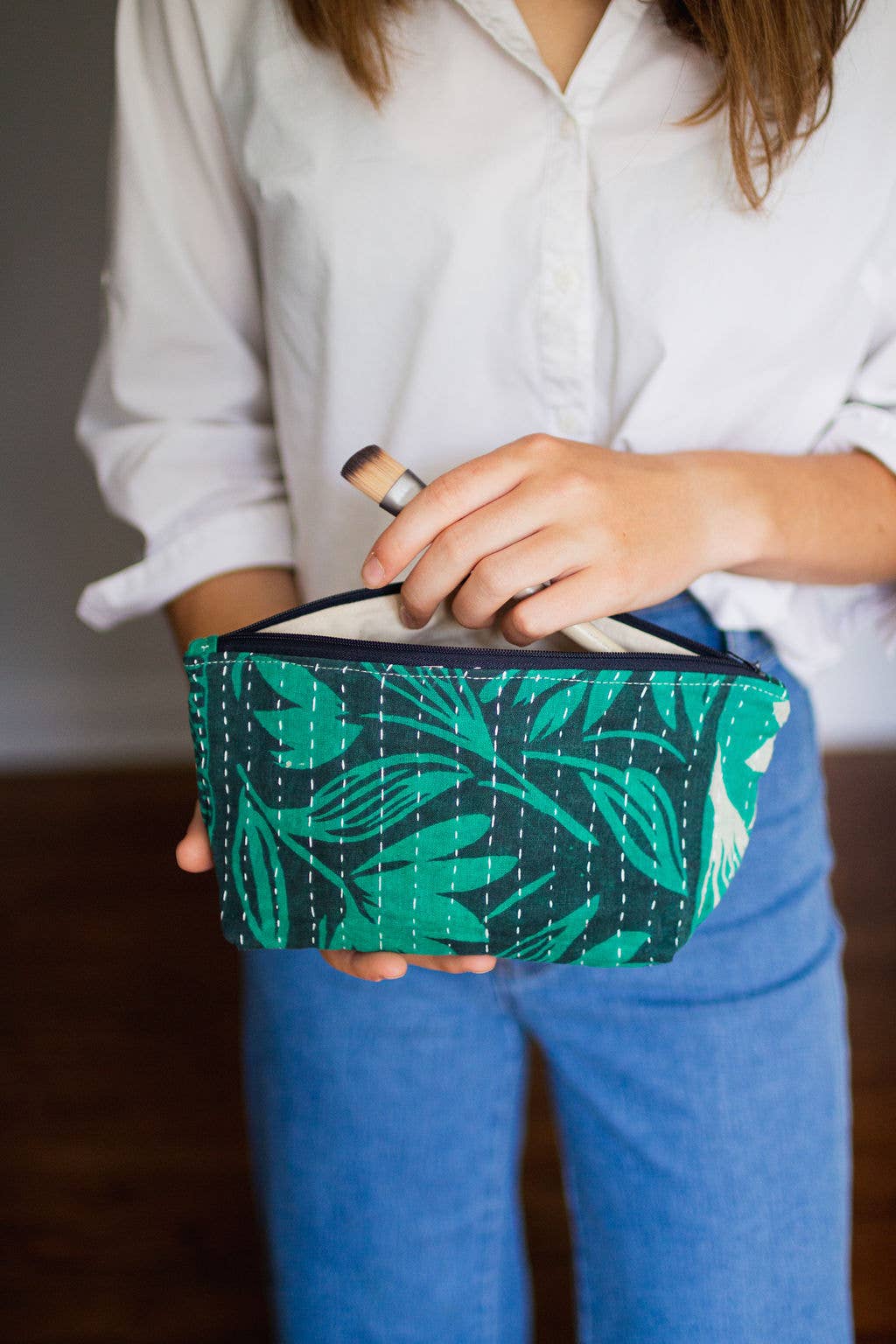 Person holding a green patterned pouch with a white interior.