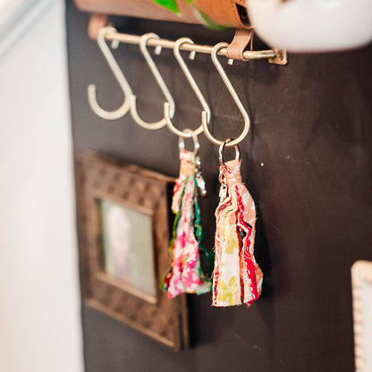 Decorative earrings hanging on a hook with a plant and picture frame in the background.