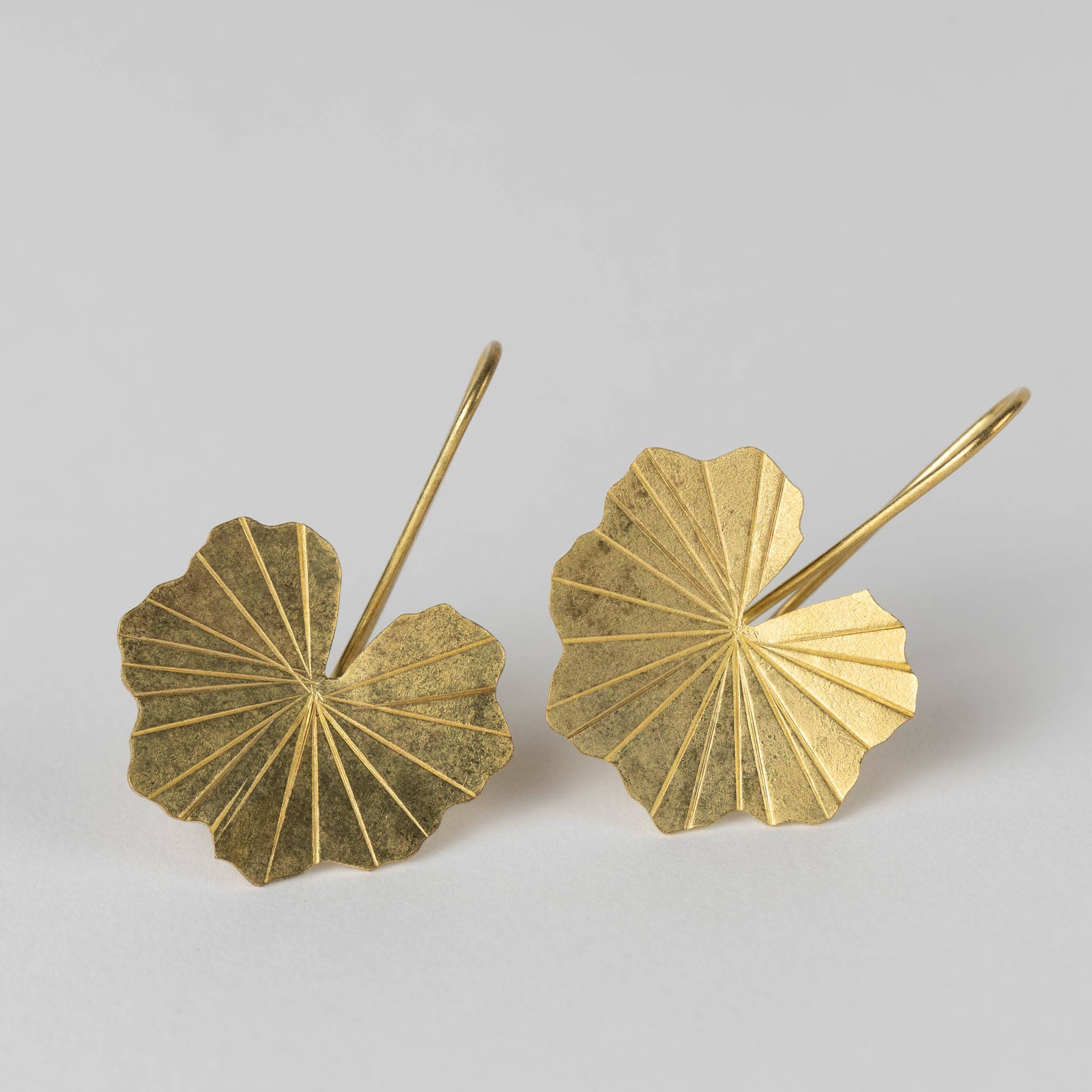 Pair of brass lotus leaf-shaped earrings on a light gray background