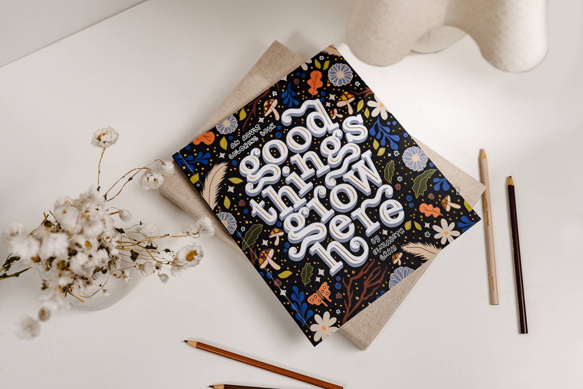 Notebook with decorative cover on a white surface with pencils and flowers