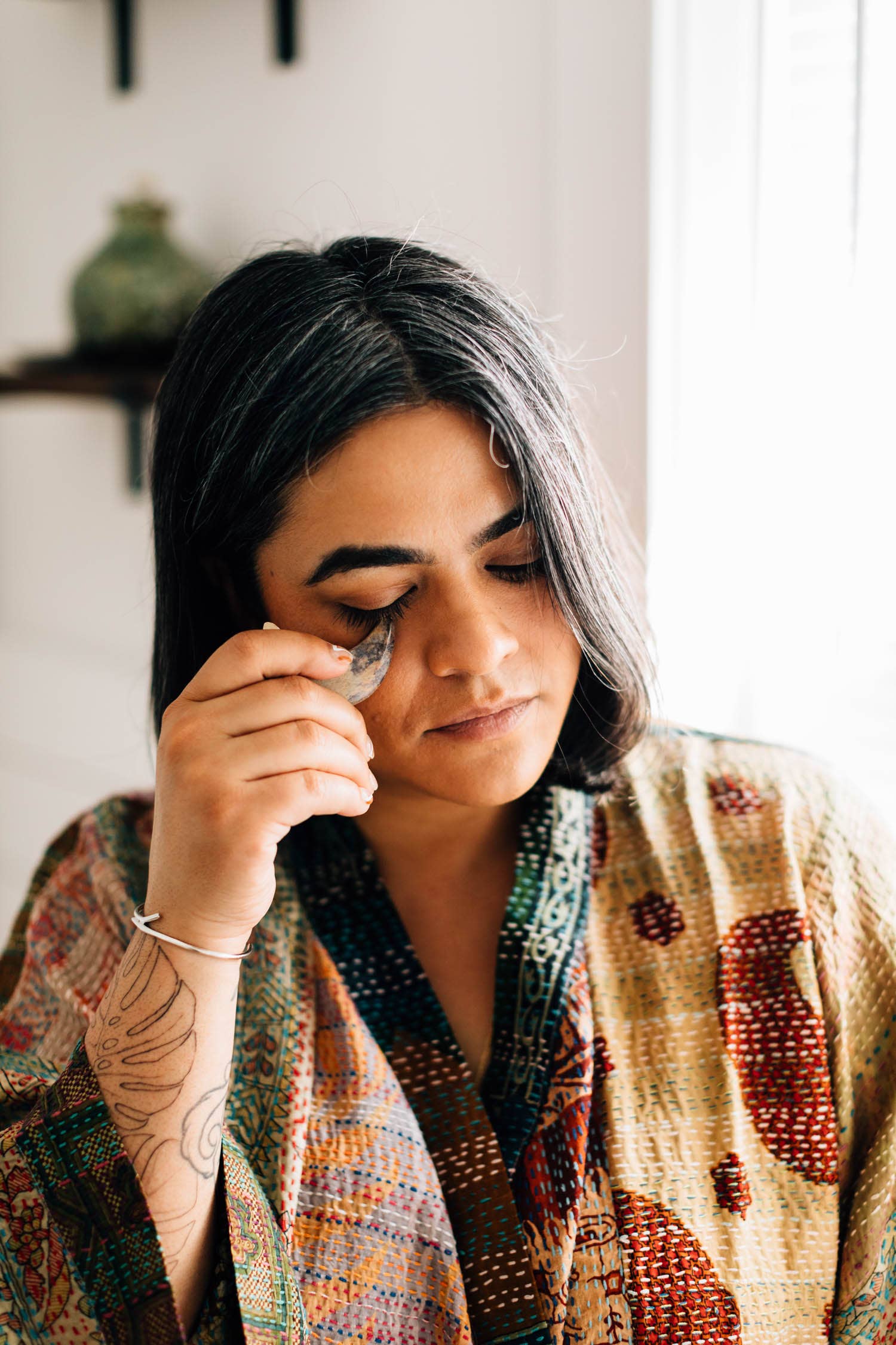 A woman is using one massage stone along cheekbone during skincare routine