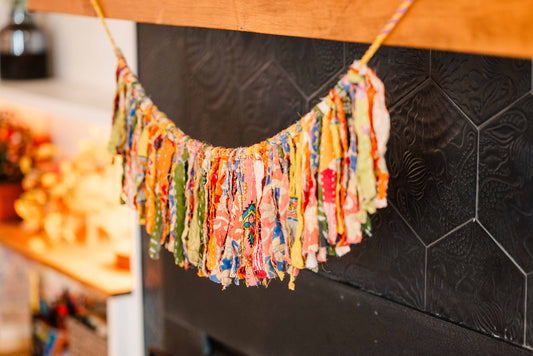 Colorful fabric tassel garland hanging on a black tiled wall.