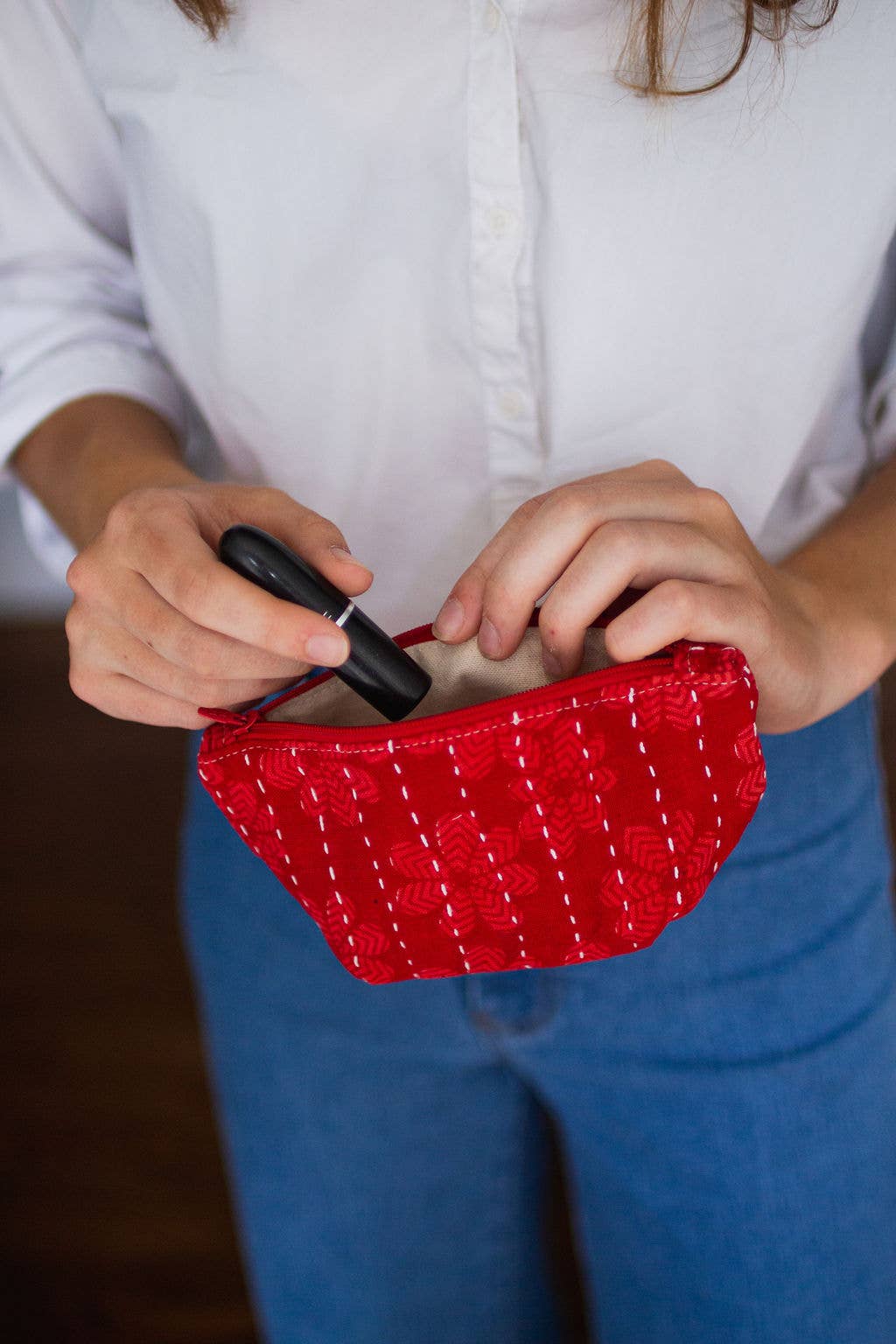 Person holding a red woven clutch with a white shirt and blue jeans.