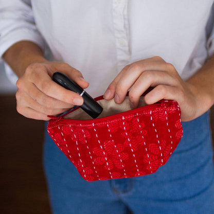 Person holding a red woven clutch with a white shirt and blue jeans.