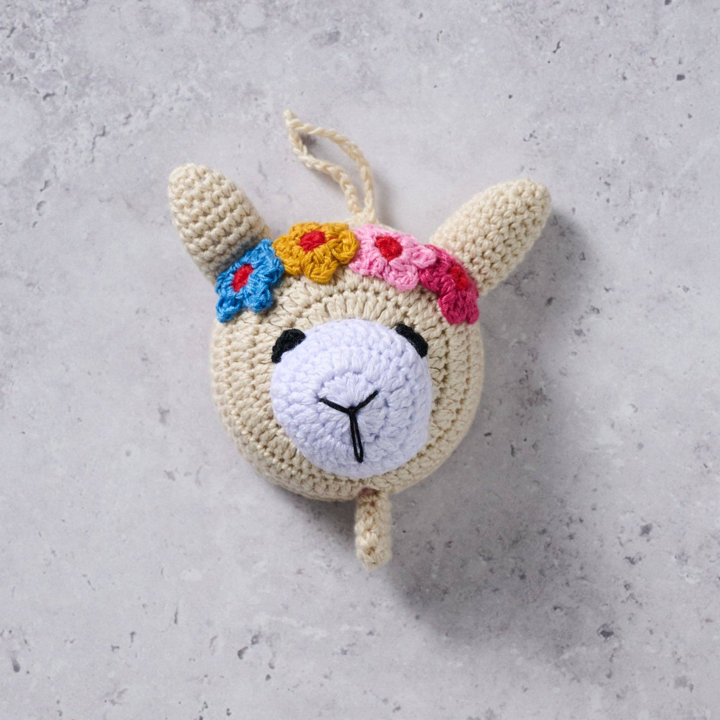 Crocheted llama toy with colorful flowers on a gray surface