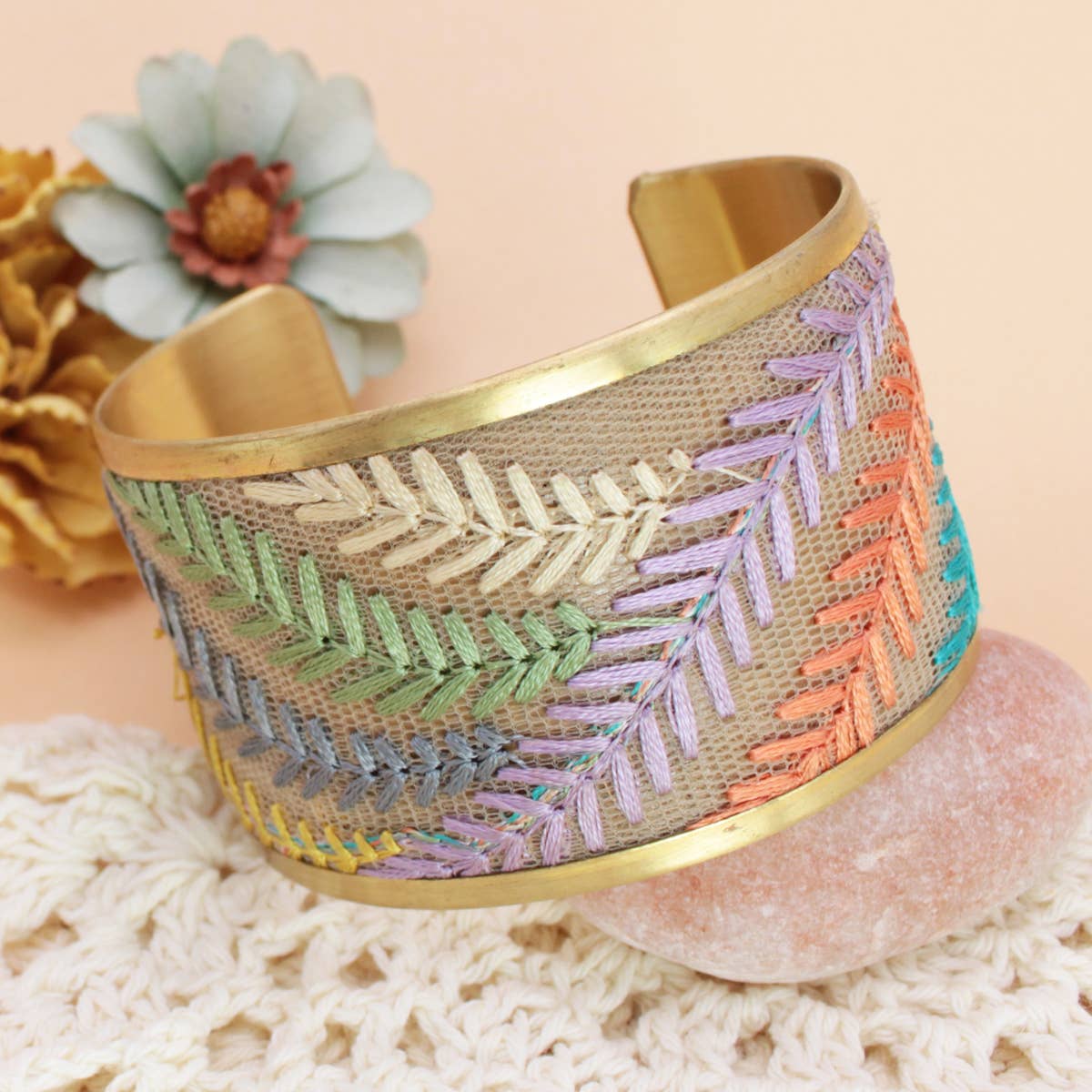 Decorative bracelet with embroidered patterns on a textured surface with flowers in the background