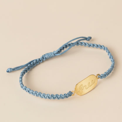 Blue braided bracelet with a gold tag on a light gray background