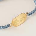 Bracelet with gold tag and blue cord on a white background