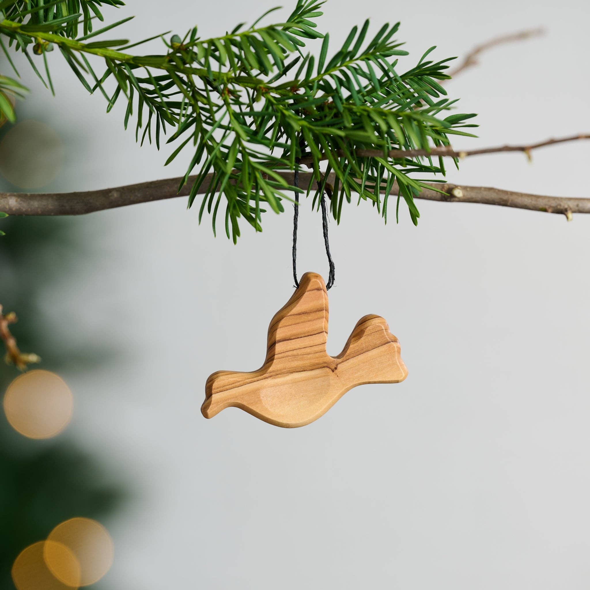 Wooden dove ornament hanging on a branch with a blurred holiday background