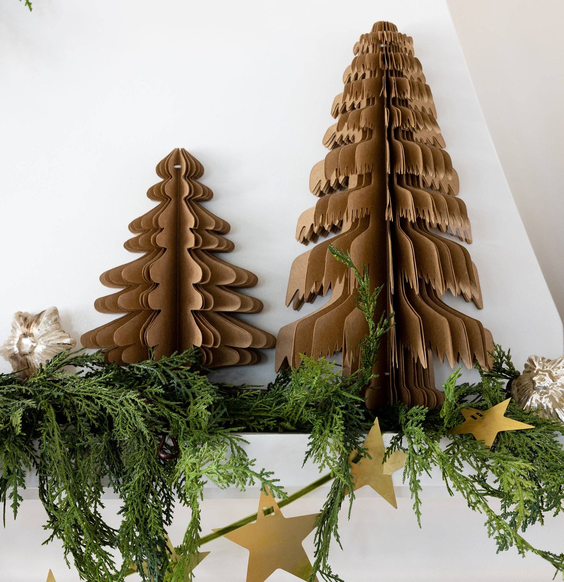 Cardboard Christmas trees on a white wall with greenery and gold stars.