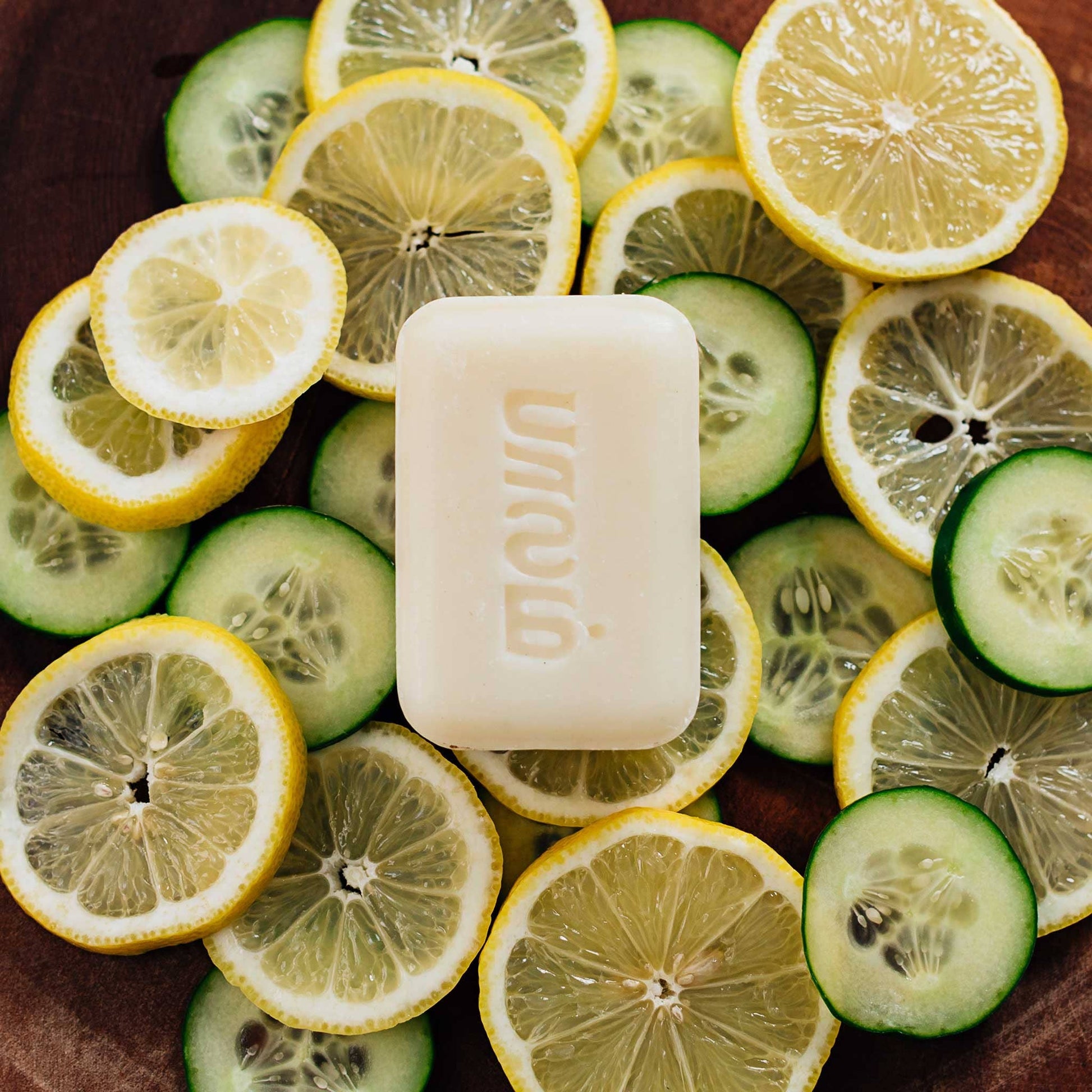 Bar of soap surrounded by sliced lemons and cucumbers on a wooden surface