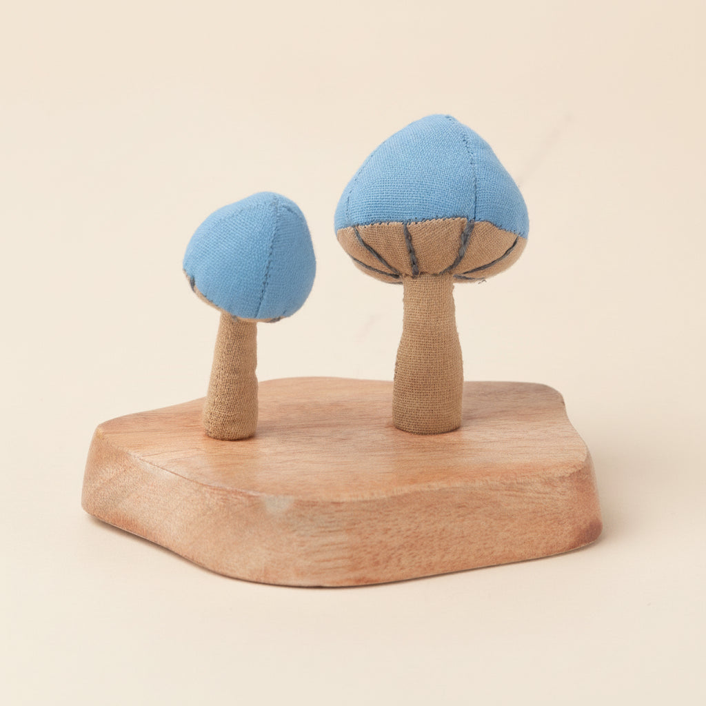Two blue and beige fabric mushrooms sprouting from a rustic wooden base