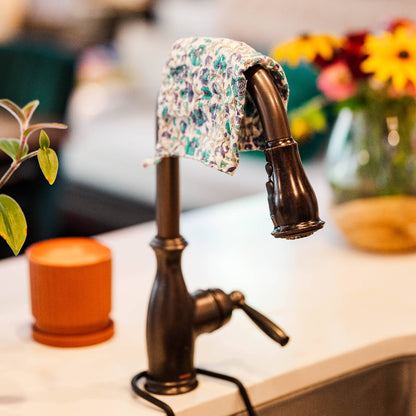 Bronze faucet with a floral-patterned cloth draped over it, set against a blurred indoor background.
