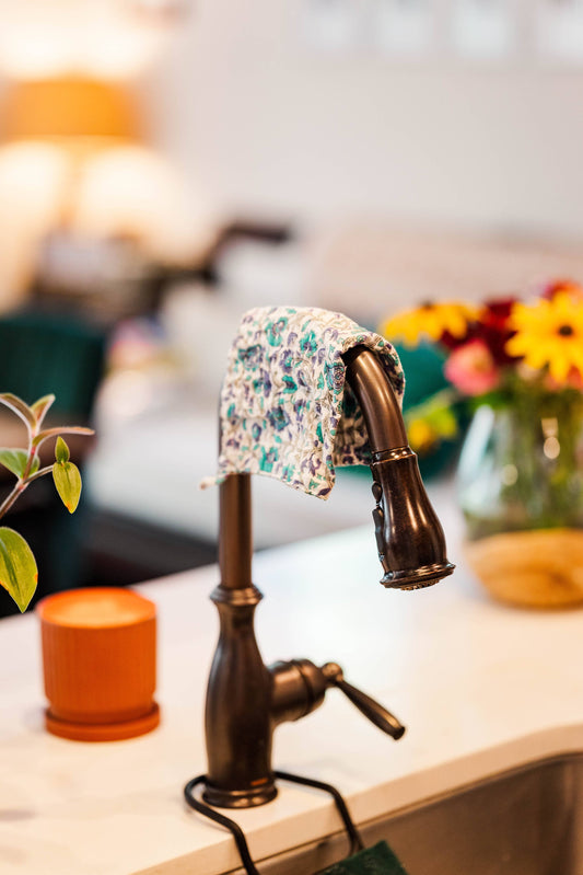 Bronze faucet with a floral-patterned cloth draped over it, set against a blurred indoor background.