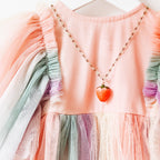 Strawberry necklace styled on a child’s pastel pink dress with ruffle sleeves, emphasizing playful charm