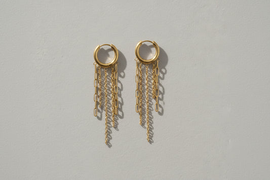 Gold chain earrings on a gold stand against a beige background